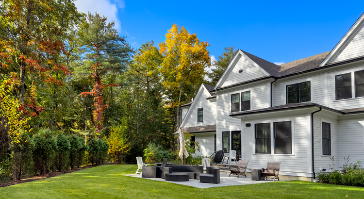 White home with a backyard patio surrounded by autumn trees